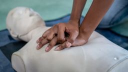 Closeup hands practicing chest compressions on a CPR training dummy.