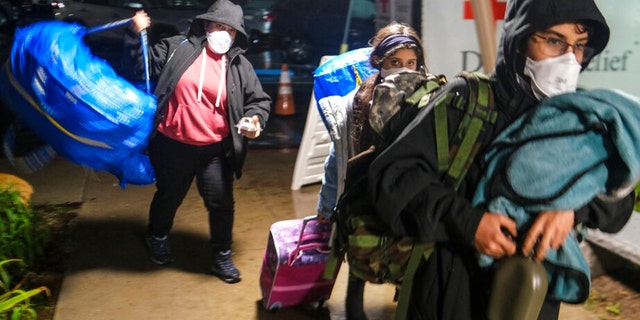 People carrying their belongs arrive at an evacuation center in Santa Barbara, Calif., Monday, Jan. 9, 2023. 