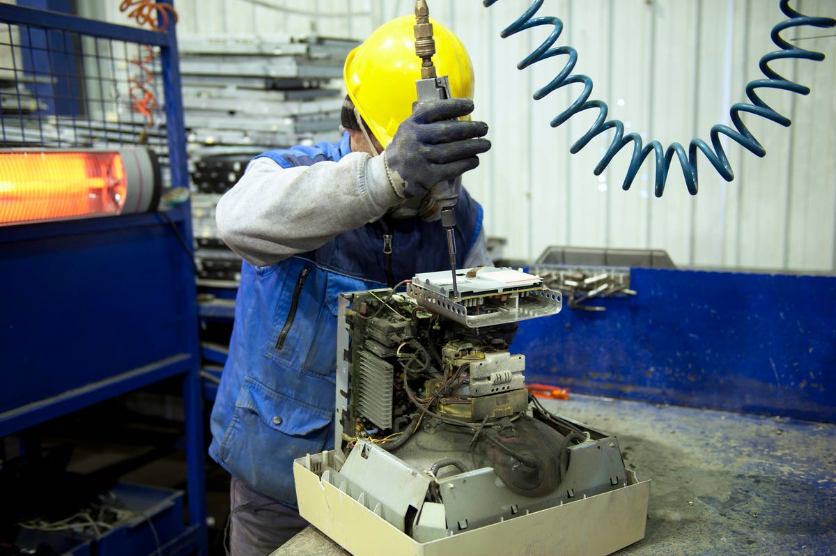 A hard-hatted worker takes apart a CRT monitor.