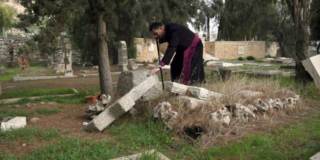 Hosam Naoum, a Palestinian Anglican bishop, touches a damaged grave where vandals desecrated more than 30 graves at a historic Protestant Cemetery on Jerusalem's Mount Zion in Jerusalem, Wednesday, Jan. 4, 2023.