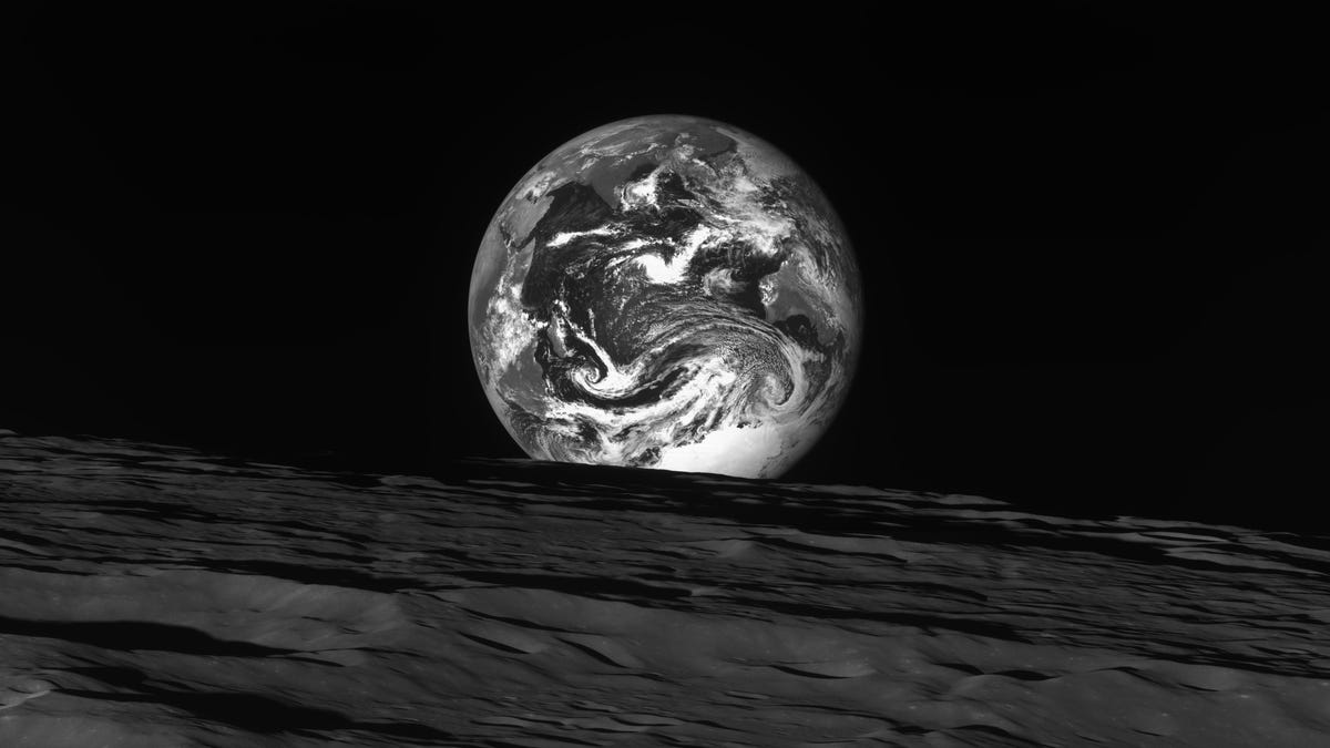 Dark moon landscape along the bottom with many crater as the Earth appears just above the horizon, all in black and white.