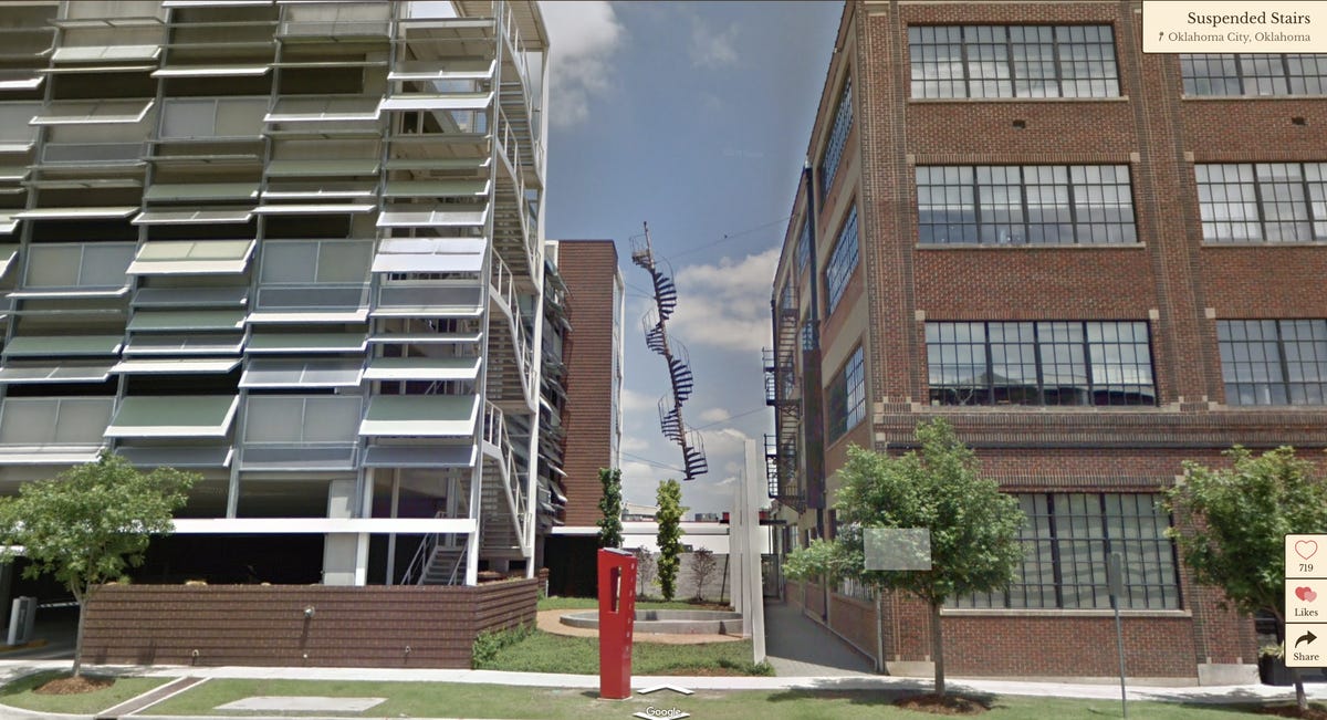 A spiral staircase appears suspended between two buildings.