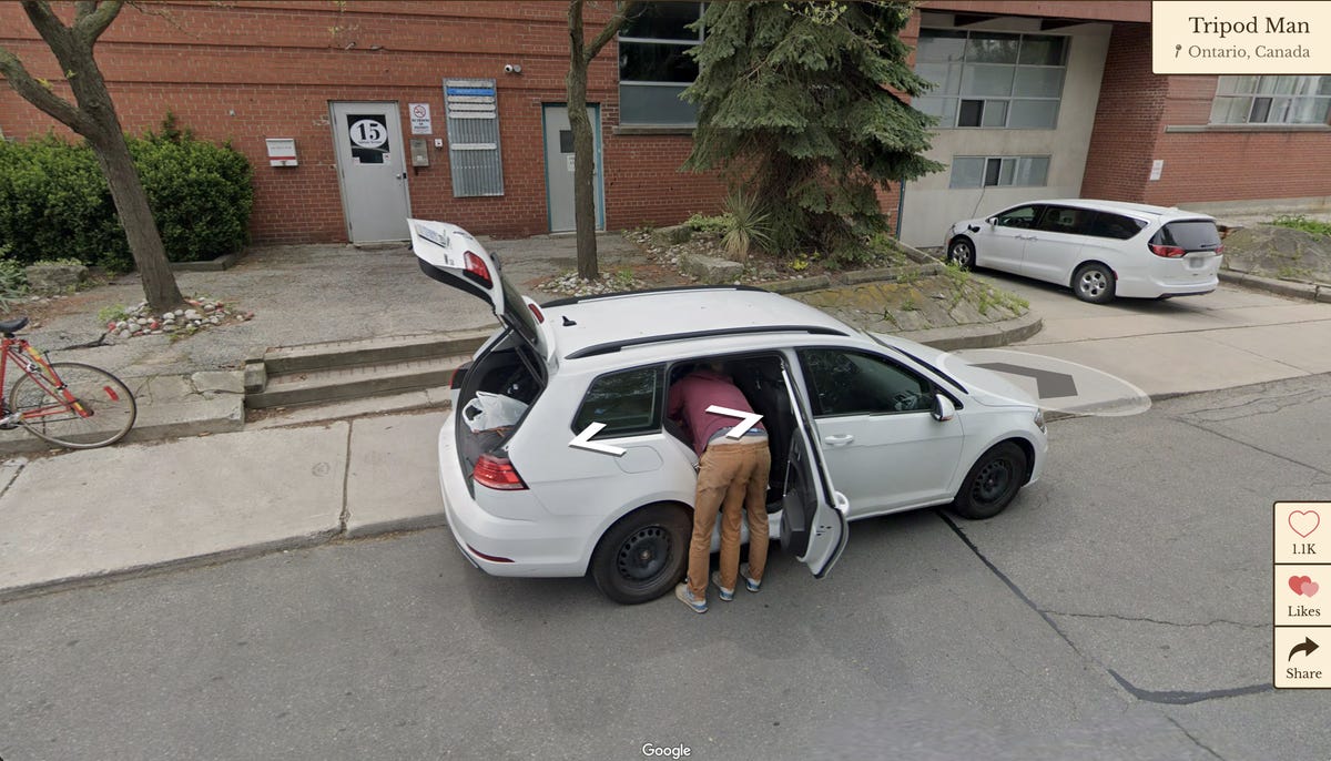 A man is seen looking in the backseat of his car, but it looks as though he has three legs.