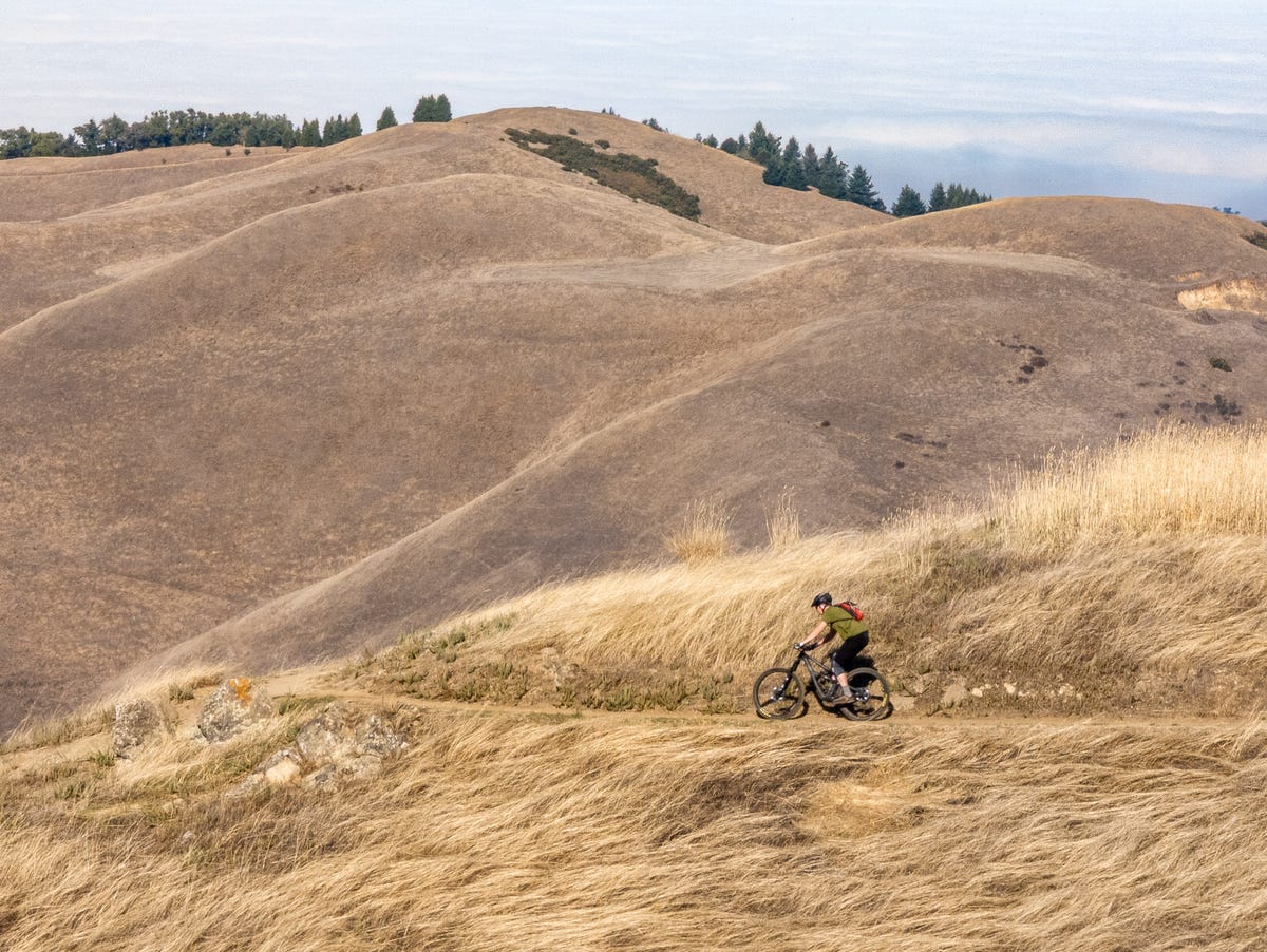 A telephoto shot of a distant mountain biker riding through wavy grass in front of rolling hills
