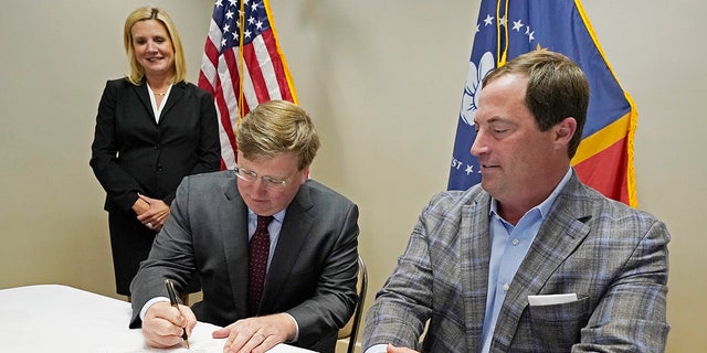 With wife Elee Reeves, left, and party Chairman Frank Bordeaux witnessing, Mississippi Gov. Tate Reeves, center, signs his qualifying papers to run for re-election at the party headquarters in Jackson Jan. 3, 2023.