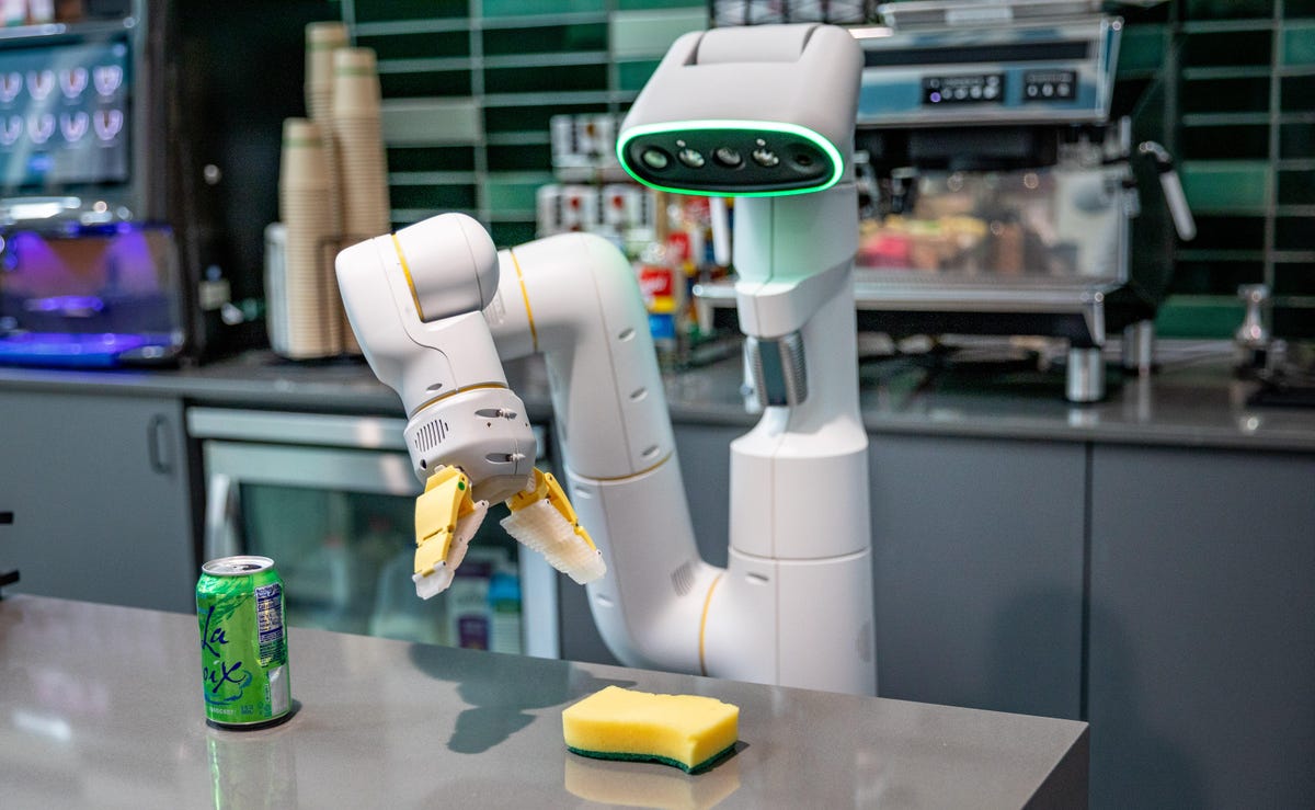 A Google robot reaches for a sponge among items on a kitchen counter