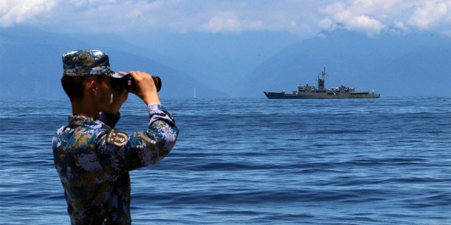 A People's Liberation Army member looks through binoculars during military exercises as Taiwan’s frigate, Lan Yang, is seen in the distance, Aug. 5, 2022.