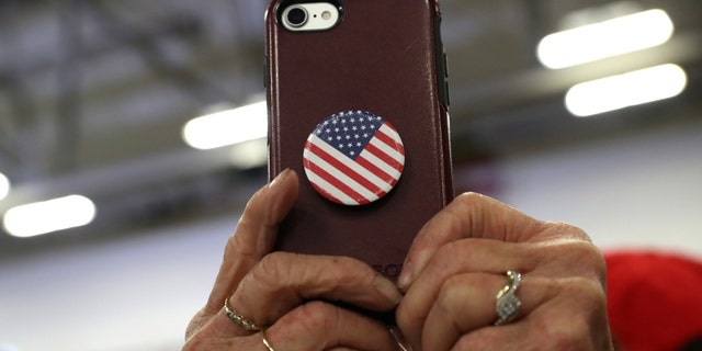 A woman holds a phone adorned with a Stars and Stripes PopSocket.