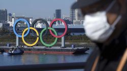 FILE - In this Dec. 1, 2020, file photo, a man wearing a protective face mask to help curb the spread of the coronavirus walks with the Olympic rings in the background in the Odaiba section in Tokyo. Opposition to the Tokyo Olympics is growing with calls for a cancellation as virus cases rise in Japan. The International Olympic Committee and local organizers have already said another postponement is impossible, leaving cancellation, or going ahead, as the only options. (AP Photo/Eugene Hoshiko, File)