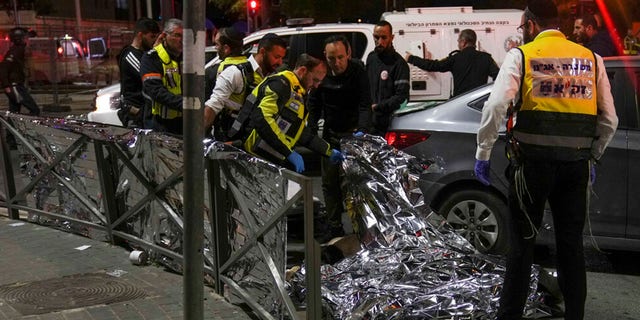 Members of Zaka Rescue and Recovery team check a body after a shooting attack near a synagogue in Jerusalem , Friday, Jan. 27, 2023. 