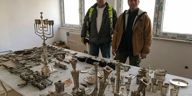 Four hundred items including silver-plated menorahs and tableware were found during the renovation of a house and yard in Poland. The recovered objects will be transferred to a museum. A building inspector, left, and an archeologist pose for a photograph with the objects in Lodz, Poland, on Jan. 11, 2023. 