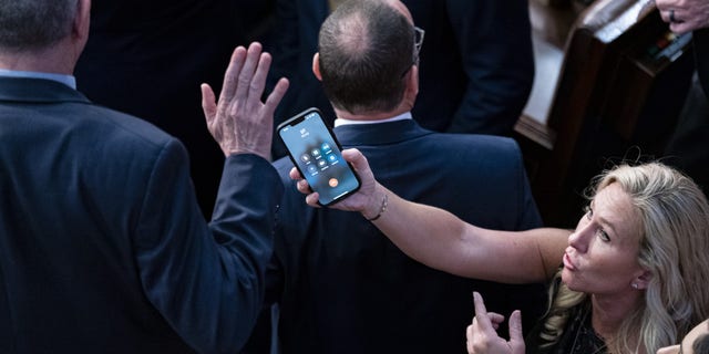 Rep. Marjorie Taylor Greene, a Republican from Georgia, holds her phone with former President Donald Trump on the line, as Rep. Matt Rosendale, a Republican from Montana, waves it off during a meeting of the 118th Congress in the House Chamber at the U.S. Capitol in Washington, D.C., Friday, Jan. 6, 2023.