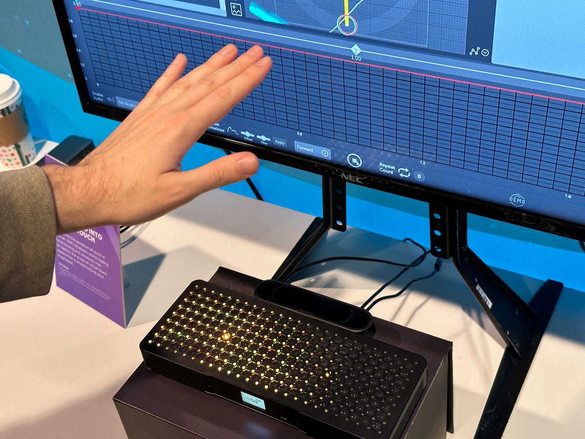 A hand over a black bar sensor, in front of a computer monitor. The sensor creates haptic feedback.