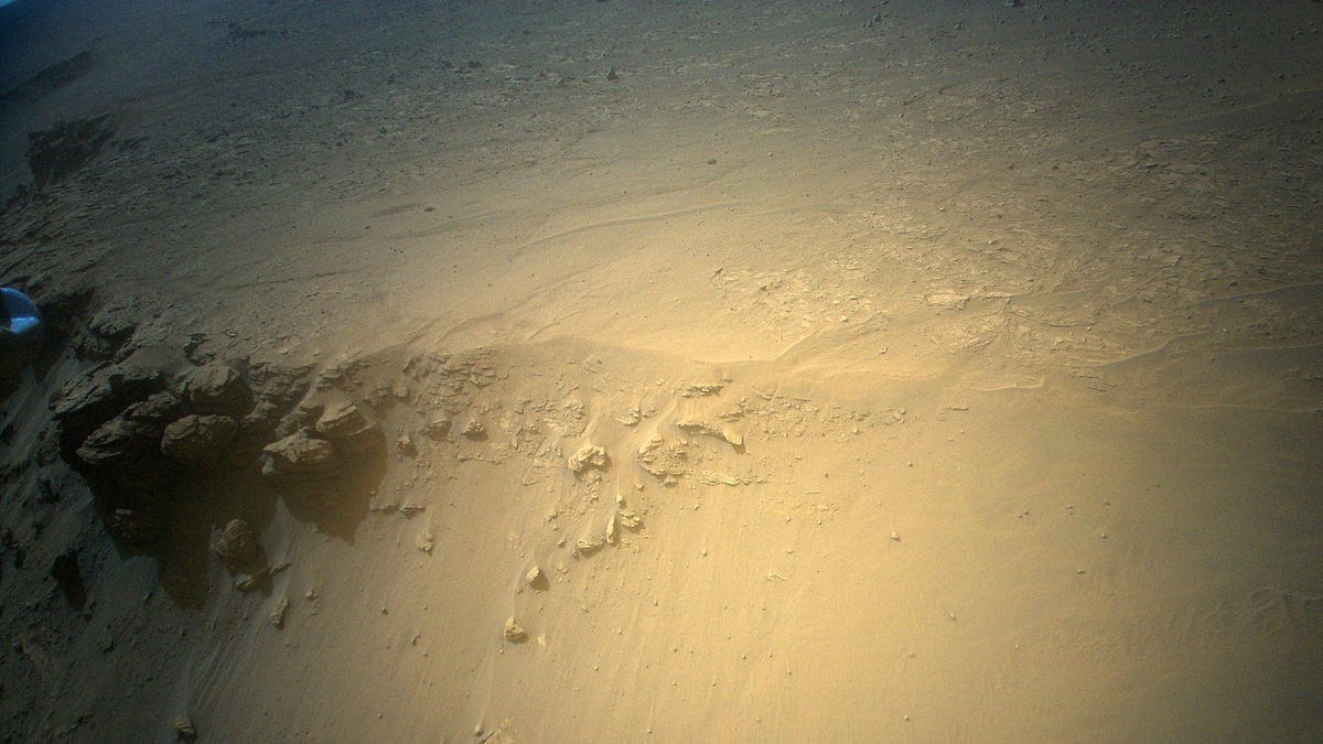 Aerial view of Mars from Ingenuity helicopter shows a low, rocky ridge and an expanse of sand.
