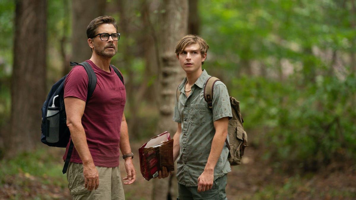 Rob Lowe as John, Johnny Berchtold as Fielding standing outside in a forest