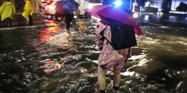 People cross a flooded street in Auckland, on Jan. 27, 2023. Record levels of rainfall pounded New Zealand's largest city over the weekend. The country's northern region expects more flooding in the coming days.