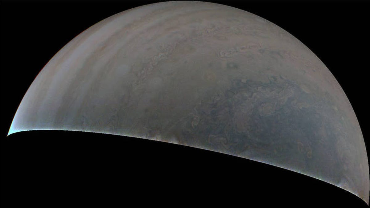 Partial view of Jupiter as seen by NASA's Juno spacecraft. Stormy swirls are visible in muted shades of blue and blush pink.