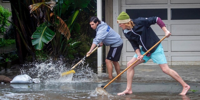 Evan Sousa, left, gets help from Calvin Drake pushing water out of his flooded apartment on Palmetto Avenue in Pacifica, Calif., on Jan. 5, 2023. 