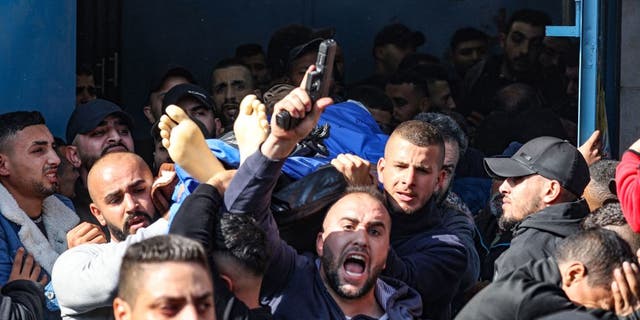 A man fires his gun into the air as Palestinians carry the body of one of the 9 reported victims killed during an Israeli raid on the West Bank's Jenin refugee camp, as they begin his funeral procession in the city of the same name on January 26, 2023. (JAAFAR ASHTIYEH/AFP via Getty Images)