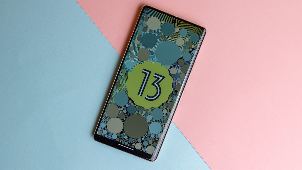 Pixel 7 Pro phone with Android 13 logo on screen, on a blue and pink background