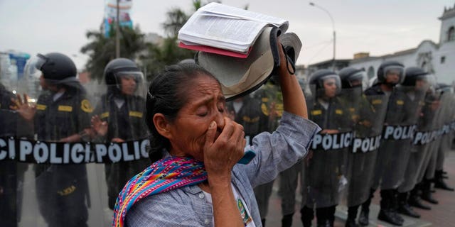 A woman carries a Bible in front of a line of riot police during a march by anti-government protesters who traveled to the capital from across the country to protest against Peruvian President Dina Boluarte in Lima, Peru, Wednesday, Jan. 18, 2023.
