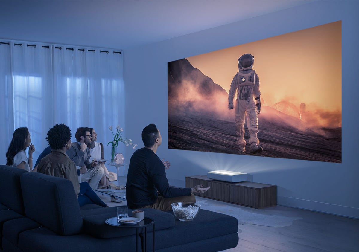 A living room with several people watching a simulated image of an astronaut on the wall created by a UST projector.