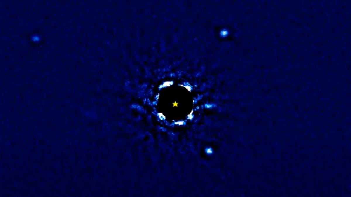 Largely dark blue screenshot shows a central star with the light blocked and four faint balls of light that are exoplanets around it.