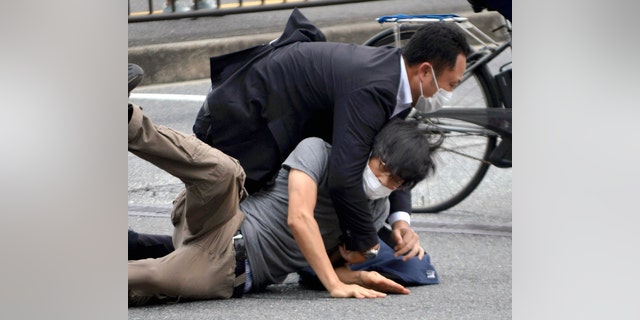 FILE - Tetsuya Yamagami, bottom, is detained near the site of gunshots in Nara Prefecture, western Japan, on July 8, 2022. Japanese prosecutors formally charged the suspect in the assassination of former Prime Minister Shinzo Abe with murder, Japan's NHK public television reported Friday, Jan. 13, 2023.