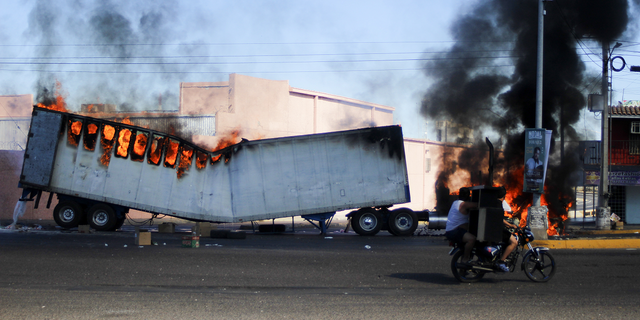 Men ride on a motorcycle past a burning truck on the streets of Culiacan, Sinaloa state, on Thursday, Jan. 5.