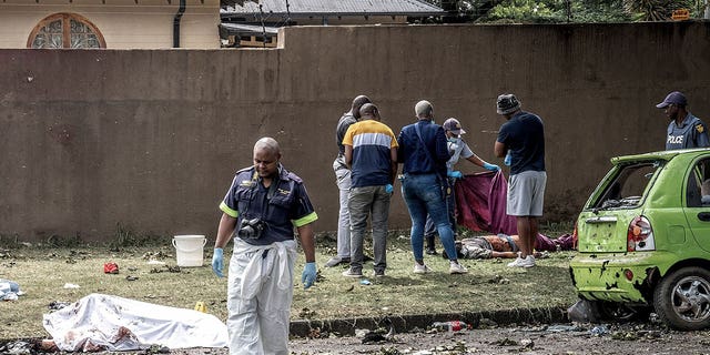 Officials and forensic experts stand beside bodies in the aftermath of a tanker explosion in Boksburg, a city east of Johannesburg, on Dec. 24, 2022.