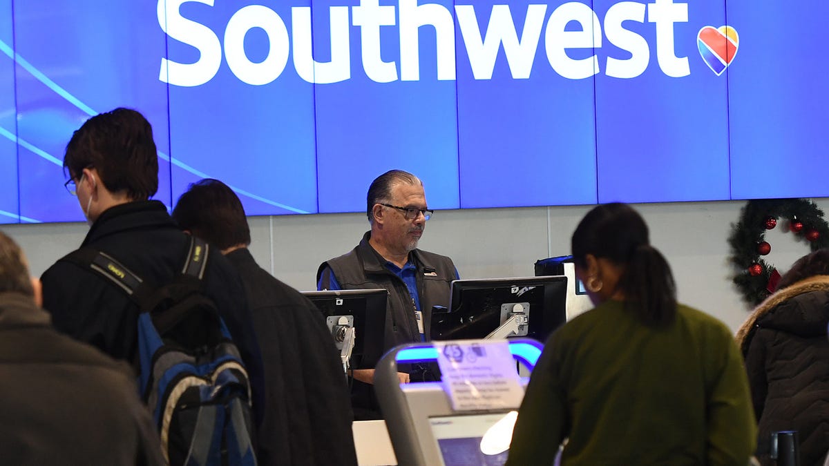 A Southwest airlines agent works at a terminal at an airport in front of a southwest airlines sign