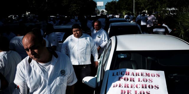 Taxi drivers walk past a sign reading, "We are fighting for the rights of the taxi drivers" during a protest against the regulation of taxi-hailing apps such as Uber in Cancun, Mexico Jan. 11, 2023. 