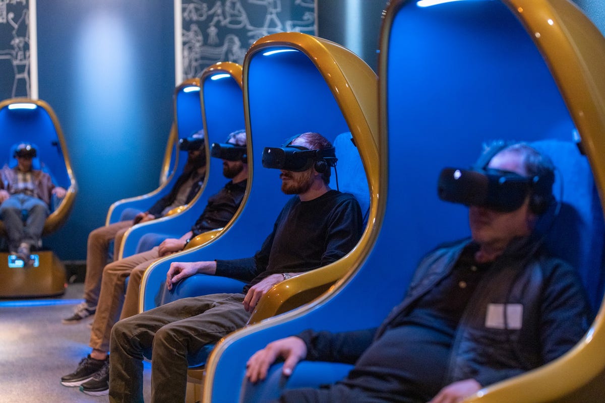Museumgoers site in curved cinematic motion chairs, with VR headsets on