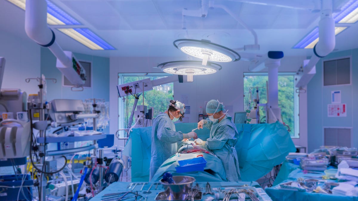 Doctors in an operating room are wearing clinical gear and performing open heart surgery on a patient.