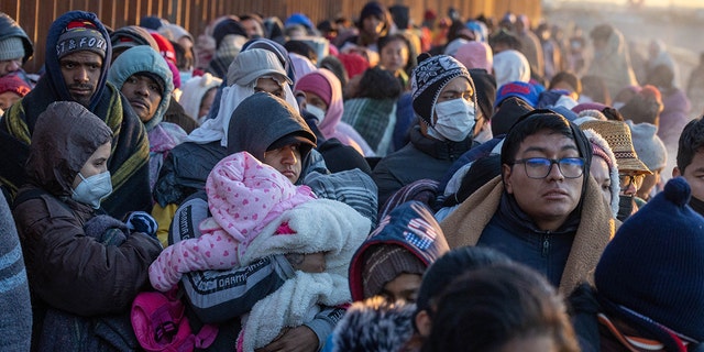 Immigrants bundle up against the cold after spending the night camped alongside the U.S.-Mexico border fence on Dec. 22, 2022, in El Paso, Texas.