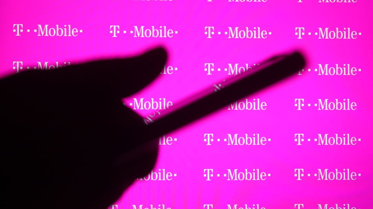 A shadow of a hand using a smartphone in front of T-Mobile logos.