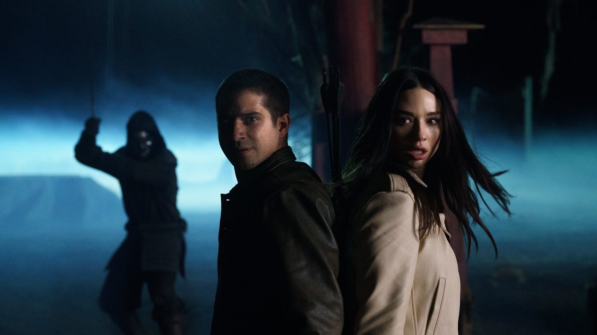 Tyler Posey as Scott and Crystal Reed as Allison stand back to back in fighting stance at night