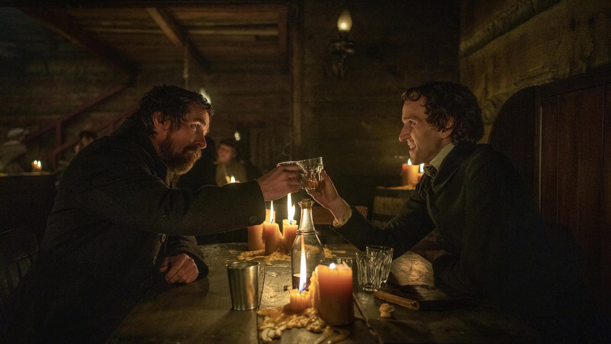 Christian Bale and Harry Melling as detective Augustus Landor and Edgar Allan Poe respectively, sitting across from each other in a candle-lit pub