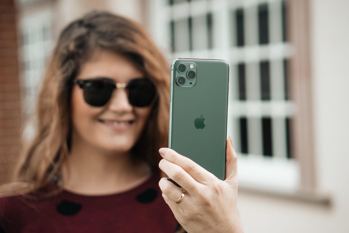 A woman in sunglasses smiling at an iPhone