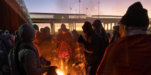 Immigrants warm by a fire at dawn after spending a night alongside the U.S.-Mexico border fence on Dec. 22, 2022, in El Paso, Texas.