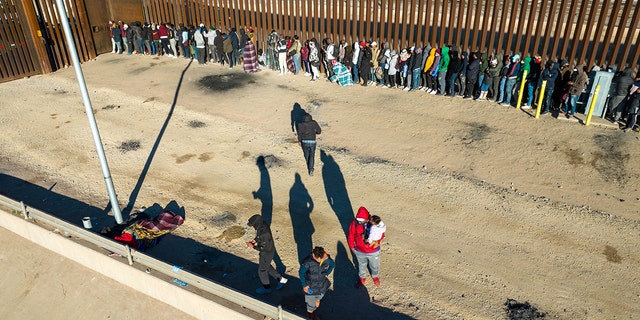 Immigrants line up next to the U.S.-Mexico border fence after spending the night outside on Dec. 22, 2022, in El Paso, Texas.