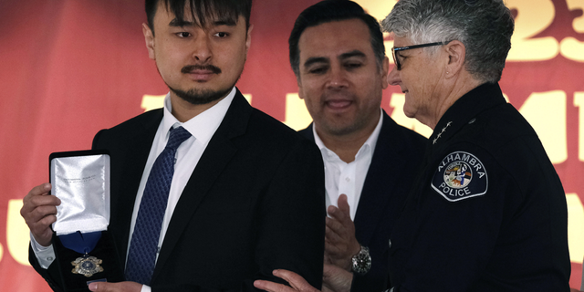 Brandon Tsay displays a Metal of Courage award after being presented to him by Alhambra Police Chief Kelley Fraser, right, on Sunday, Jan. 29, 2023 in Alhambra, California