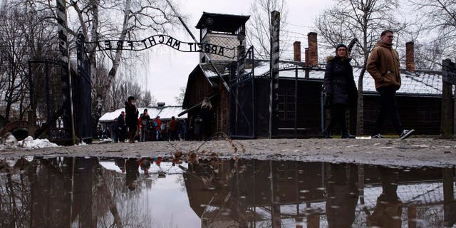 People walk next to the ''Arbeit Macht Frei" (Work Sets You Free) gate at the former Nazi German concentration and extermination camp Auschwitz-Birkenau in Oswiecim, Poland, Thursday, Jan. 26, 2023.