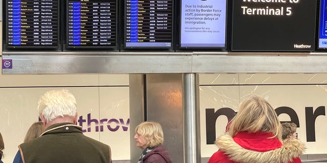 People stand near an arrivals board which displays a message warning users of Terminal 5 about industrial action by Border Force staff, at Heathrow Airport, near London Dec. 23, 2022.  