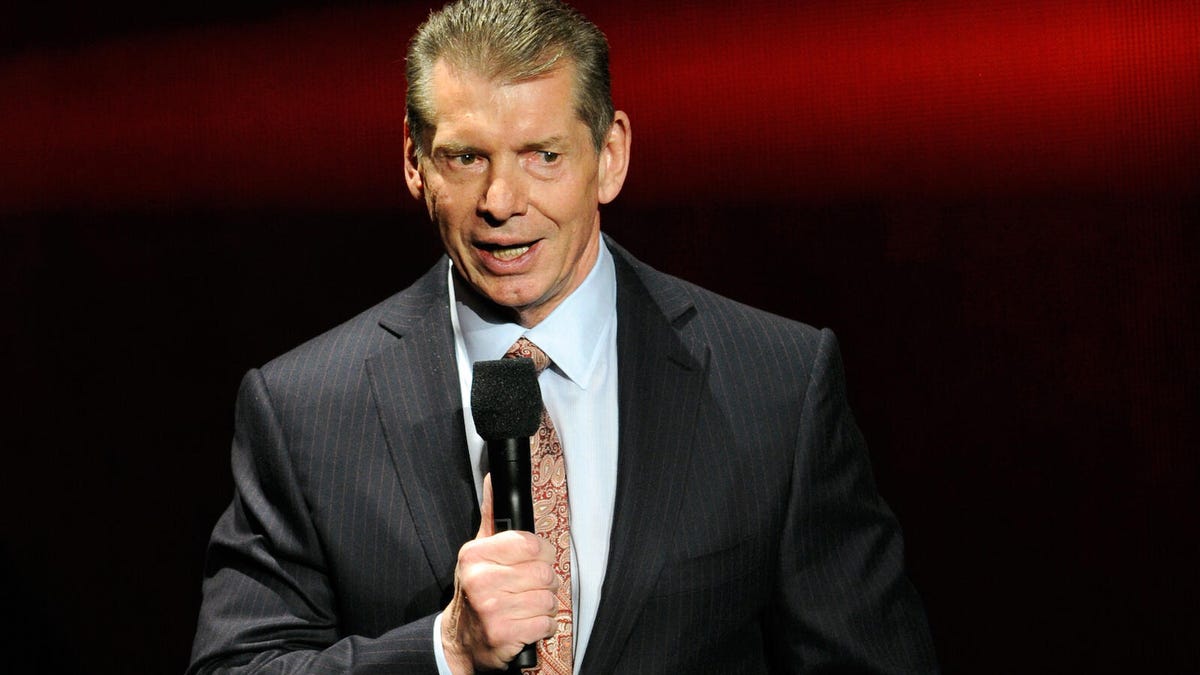 WWE promoter and former CEO Vince McMahon in a suit and speaking in a microphone.