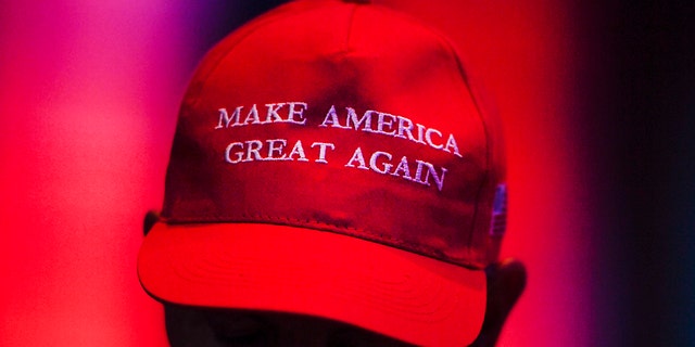 A person is photographed wearing a MAGA hat during a conference.