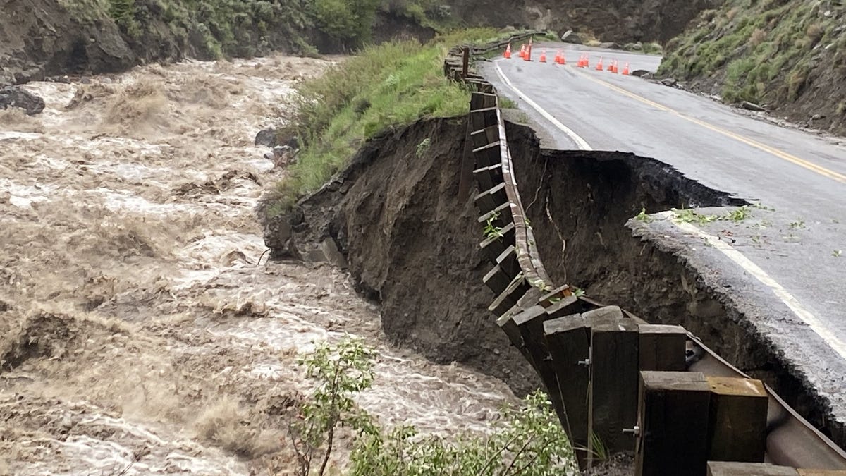 A road with missing asphalt next to a roiling stream