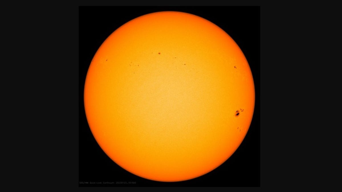 Sun as an orange disc against darkness. There's a notable blotchy dark sunspot on the far right.