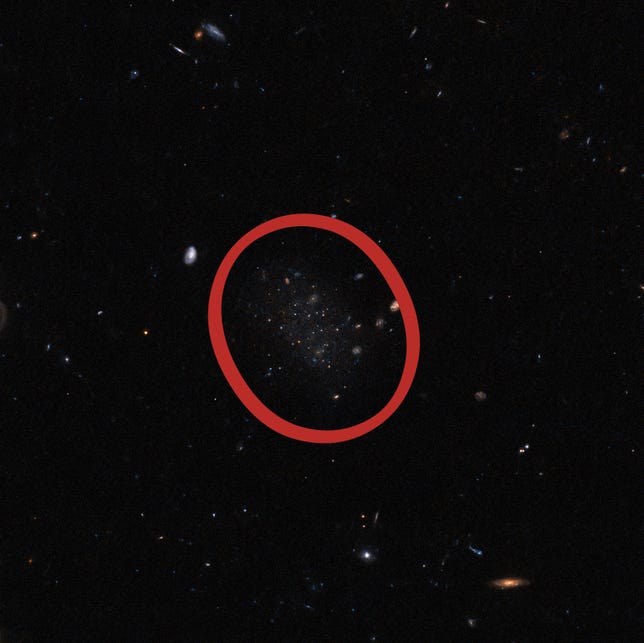 Hubble telescope image of a dark expanse of space with stars and distant galaxies, a vague, smudgy section in the middle represents the stars of galaxy Donatiello II.