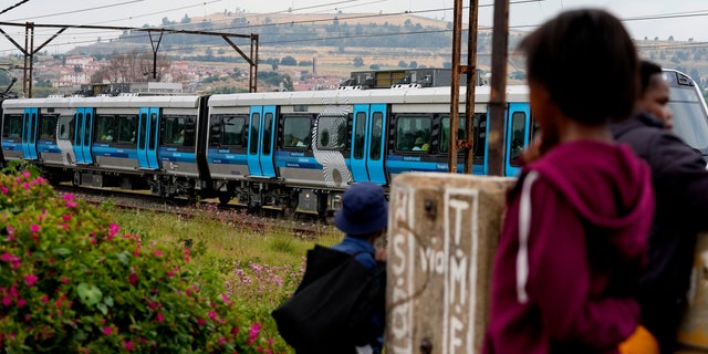 Pedestrians watch a train traveling from Johannesburg to Naledi in Soweto, South Africa, Wednesday, Feb. 8, 2023.